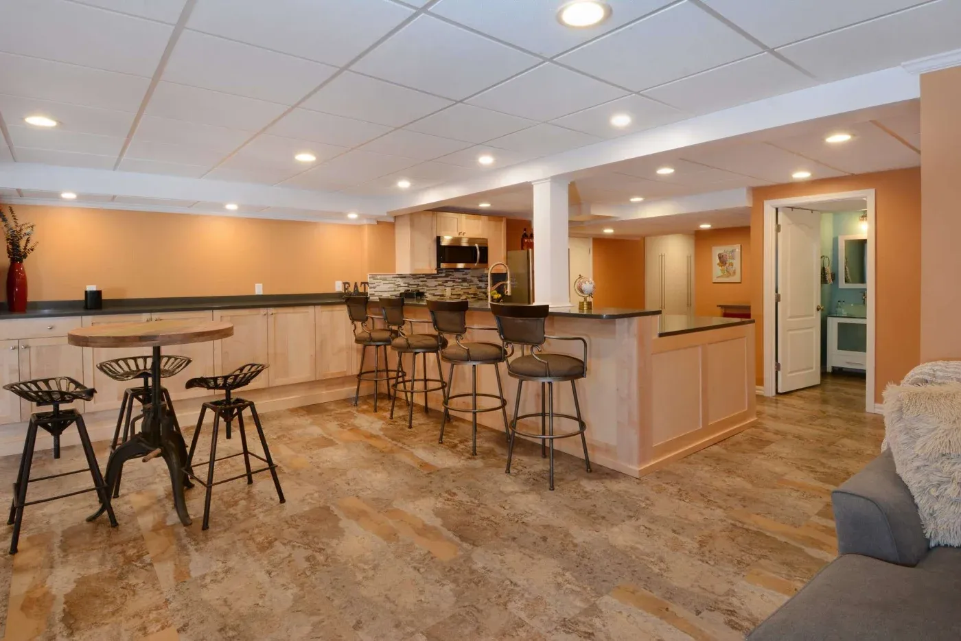 Modern basement bar with warm lighting, bar counter, and high stools. Cozy seating area and rustic decor create an inviting and stylish atmosphere.
