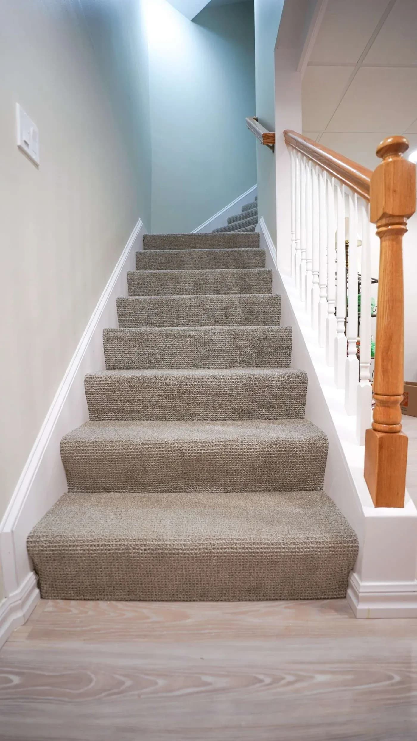 Carpeted staircase ascending with white walls and wooden handrail, creating a cozy and inviting atmosphere. Soft lighting from above enhances the welcoming feel.