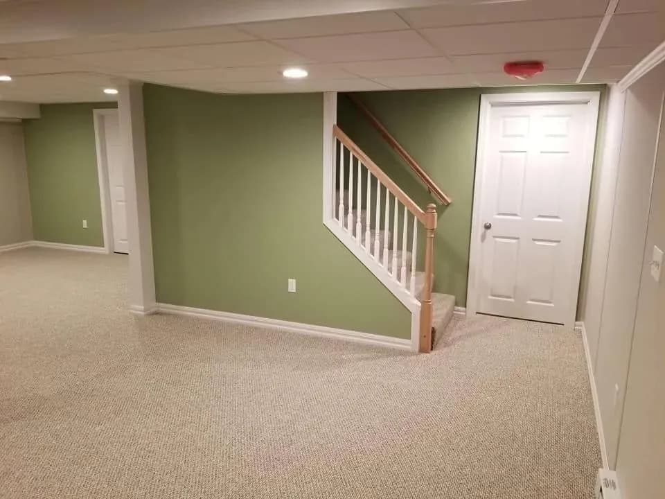 Finished basement with green accent walls, carpeted floor, wooden stair railing, white closet doors, and recessed lighting