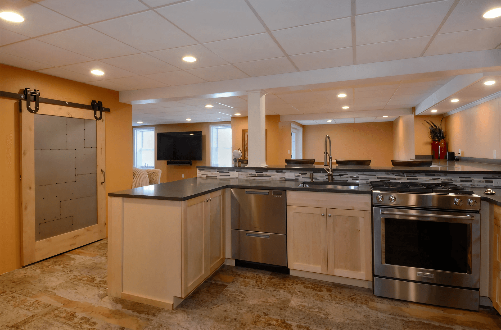 Modern kitchen with stainless steel appliances, light wood cabinets, and a dark countertop. A sliding barn door adds rustic charm to the warm, inviting space.