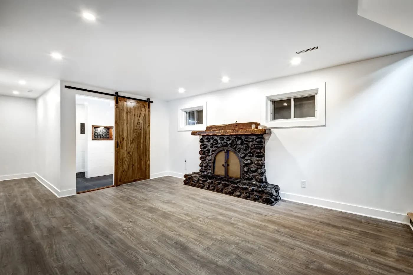 Spacious room with white walls, a rustic stone fireplace, and wooden barn door. The tone is warm and inviting with modern lighting.