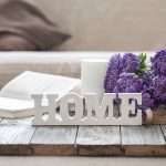 A wooden “Home” sign sitting on a table with lavender in the background