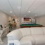 A spacious, white-walled basement with a large curved white couch in front of a home theater.